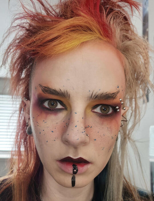 Profile picture of the editor wearing elaborate, gothic makeup. They have multicolored red hair.